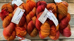 Garn i varma nyanser – teija - Textil i Järfälla Närbild på garnhärvor i orangea och röda toner på träbord – teija - Textil i Järfälla